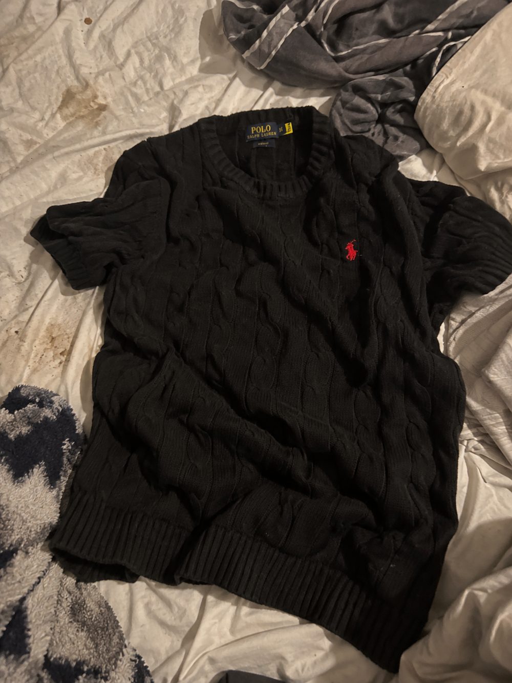 A black Polo Ralph Lauren cable knit crumpled on an unmade bed